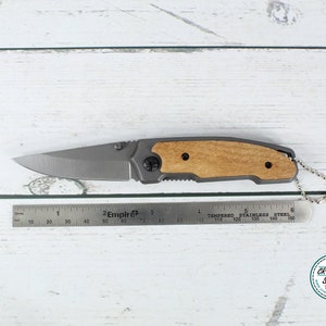 May include: A silver pocket knife with a wood handle and a keychain. The knife is 8.5 inches long and has a partially serrated blade.