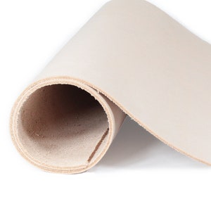 May include: A rolled-up piece of off-white leather, showcasing a smooth, unblemished surface. The edges reveal the natural, light brown color of the leather. This image highlights the texture and quality of the material, suitable for crafting projects.