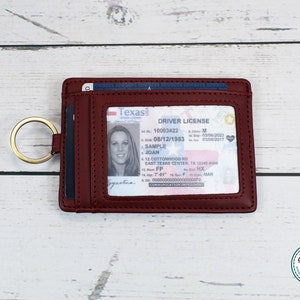May include: A burgundy leather wallet with a clear window for a driver's license. The wallet has a gold key ring attached to it. The driver's license is from Texas and shows the name "SAMPLE JOAN".