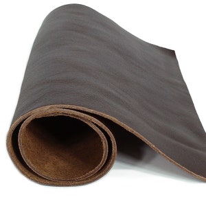 May include: A rolled sheet of dark brown leather. The leather has a textured surface and a natural, organic appearance. The edges of the leather reveal a lighter brown color, indicating the underside of the material. The leather is likely suitable for crafting.