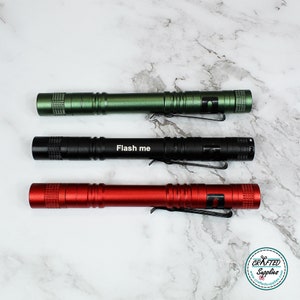 May include: Three small, pocket-sized flashlights in green, black, and red. The black flashlight has the words "Flash me" engraved on it.