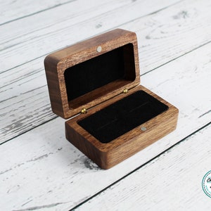 May include: A wooden ring box with a black velvet interior. The box is open and the lid is propped up.