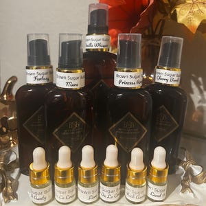 May include: A collection of five amber glass pump bottles labeled Brown Sugar Baby with scents Fantasy, Muva, Vanilla Whisper, Princess Rose, and Cherry Bomb, alongside six small glass dropper vials labeled with various scent names.