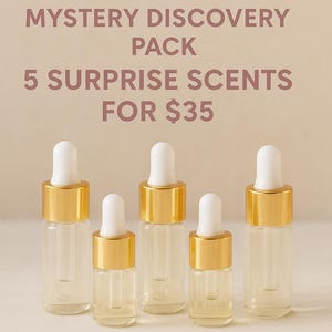 May include: Five clear glass vials with gold collars and white dropper tops containing perfume oil. The text reads: MixHer MYSTERY DISCOVERY PACK 5 SURPRISE SCENTS FOR $35 BROWN SUGAR BABE PERFUME OIL SAMPLES. The vials are arranged in a row.