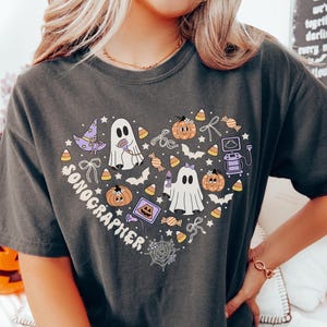 Peut inclure: Un t-shirt gris anthracite avec un motif en forme de cœur portant le texte SONOGRAPHER. Le design comprend des fantômes blancs, des citrouilles orange, des chapeaux de sorcière violets, des bonbons, des chauves-souris et une échographie.