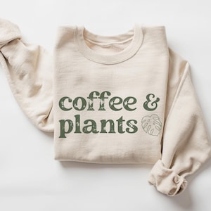 May include: A beige sweatshirt with the text "coffee & plants" in green lettering and a green leaf graphic.