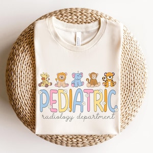 May include: Cream-colored t-shirt featuring a row of cartoon animals: giraffe, lion, elephant, monkey, and tiger. Below the animals, the word "PEDIATRIC" is written in colorful letters, with "radiology department" underneath.
