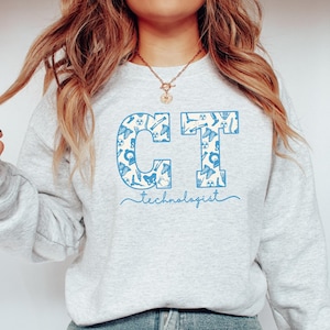 May include: A grey sweatshirt with a blue and white design of the letters "CT" with medical symbols inside the letters. The text "technologist" is written below the letters.