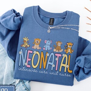 May include: A blue crewneck sweatshirt featuring a graphic of five cartoon animals including a giraffe, lion, elephant, monkey, and tiger. Below the animals, the text reads NEONATAL intensive care unit nurse in colorful, bubbly letters.