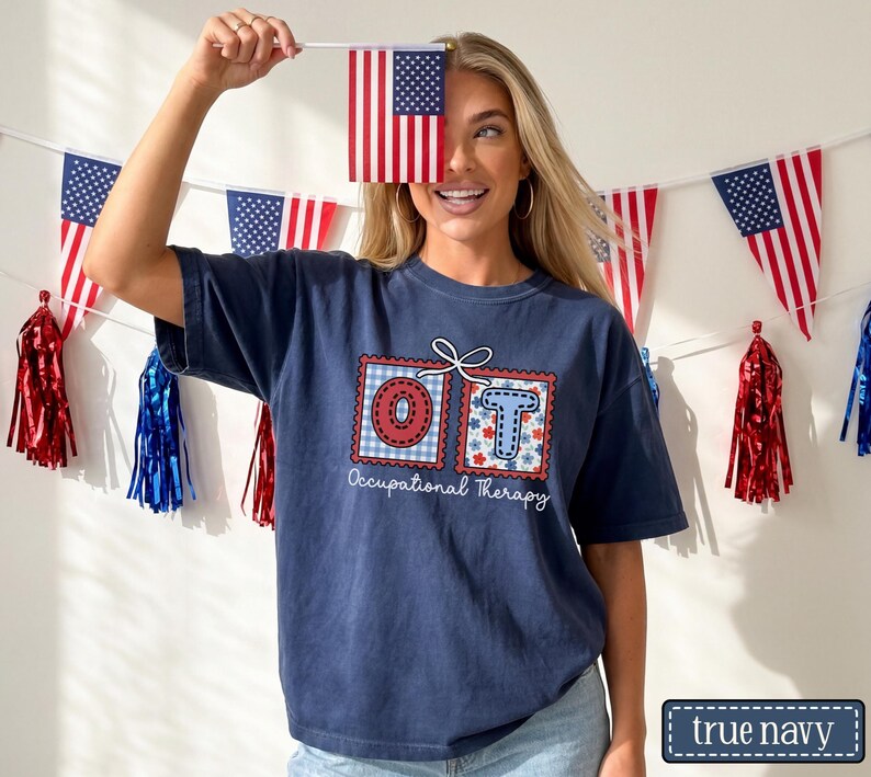 May include: Navy blue t-shirt with a graphic that says "OT Occupational Therapy" in a red and blue design. The image also includes American flag decorations and a small American flag.