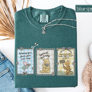 May include: A teal Comfort Colors t-shirt with three framed illustrations featuring Winnie the Pooh characters. The illustrations include text that reads "helping you grow your own way," "Speech Therapy," and "Communication looks different for everyone." A silver necklace is draped across the shirt.