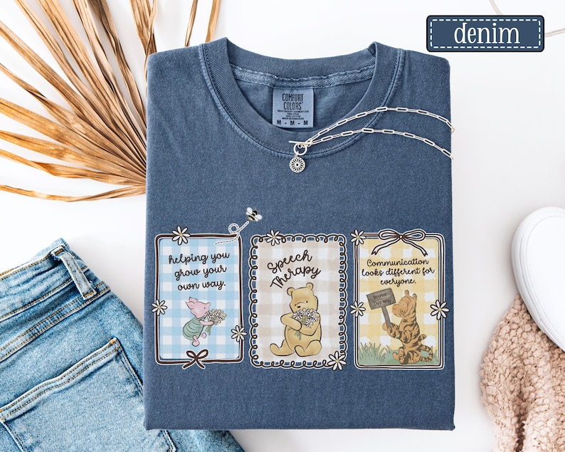 May include: Denim blue Comfort Colors t-shirt with three framed illustrations featuring Winnie the Pooh characters. The frames contain text: "helping you grow your own way," "Speech Therapy," and "Communication looks different for everyone."