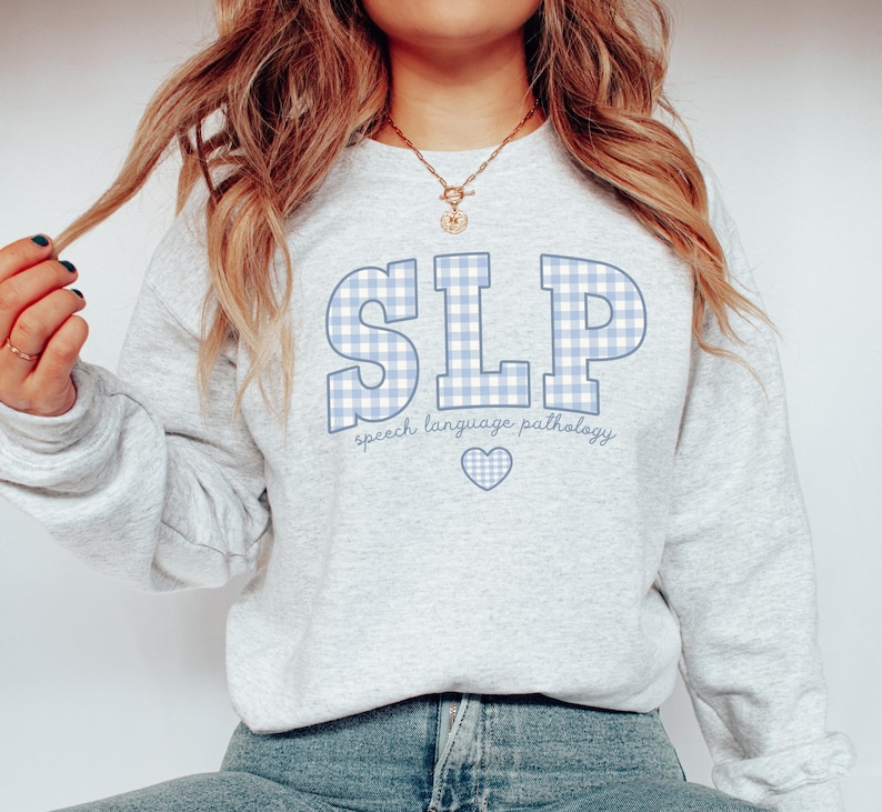 May include: A light gray sweatshirt with a blue and white gingham pattern spelling "SLP" and the text "speech language pathology" below. A small blue heart is centered below the text.