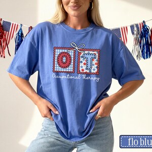 May include: A blue t-shirt with the letters "OT" in decorative postage stamp designs. The "O" is red and white checkered, and the "T" is blue with floral accents. The words "Occupational Therapy" are below the letters.