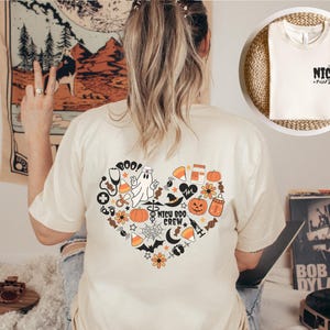 May include: Cream-colored t-shirt with a heart-shaped graphic on the back, featuring Halloween-themed illustrations and the text "NICU Boo Crew." A smaller image shows a t-shirt with the words "NICU nurse."