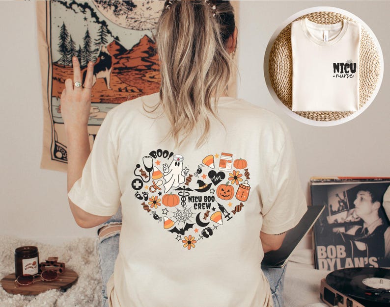 May include: Cream-colored t-shirt with a heart-shaped graphic on the back, featuring Halloween-themed illustrations and the text "NICU Boo Crew." A smaller image shows a t-shirt with the words "NICU nurse."
