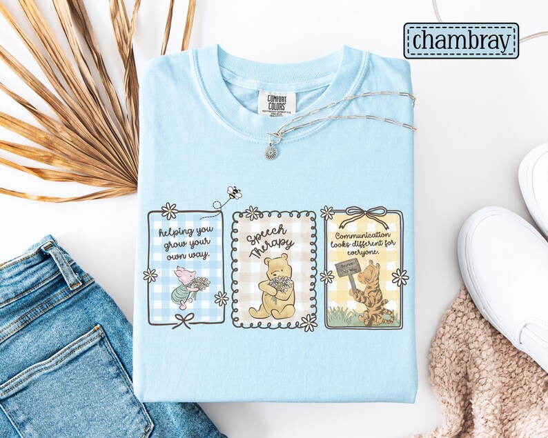 May include: Light blue Comfort Colors t-shirt featuring three framed illustrations with Winnie the Pooh characters. The frames contain the phrases: "helping you grow your own way," "Speech Therapy," and "Communication looks different for everyone."