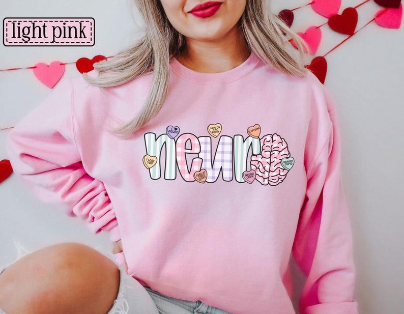 May include: A light pink sweatshirt with the word "neur" in a colorful, patterned design, accompanied by a brain graphic and heart-shaped candies. The text "light pink" is in a box in the upper left corner.