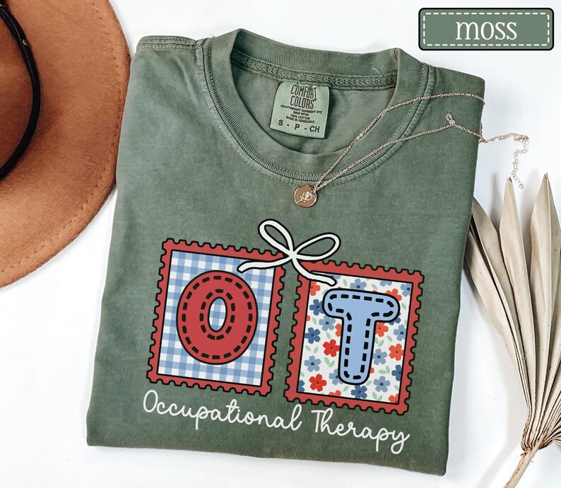May include: Moss green t-shirt with the letters "OT" in red and blue postage stamp designs. The "O" has a red gingham pattern, and the "T" has a floral pattern. The words "Occupational Therapy" are printed below the letters.