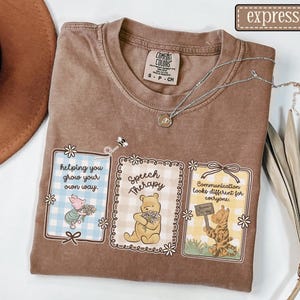 May include: Brown Comfort Colors t-shirt with three framed illustrations featuring Winnie the Pooh characters. The frames have text that reads "helping you grow your own way," "Speech Therapy," and "Communication looks different for everyone."