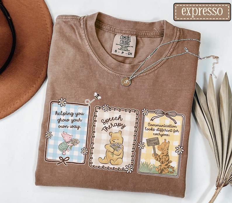 May include: Brown Comfort Colors t-shirt with three framed illustrations featuring Winnie the Pooh characters. The frames have text that reads "helping you grow your own way," "Speech Therapy," and "Communication looks different for everyone."