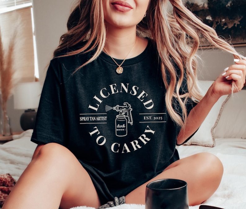 May include: Black t-shirt with a white circle graphic that says "Licensed to Carry" with a spray tan gun and bottle of "dark" tan. The text also says "Spray Tan Artist" and "Est. 2025".