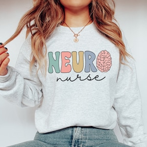 Puede incluir: Una sudadera gris claro con el texto "NEURO nurse" en letras de colores y un gr&aacute;fico de cerebro rosa.