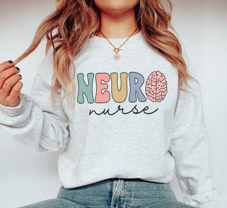 Puede incluir: Una sudadera gris claro con el texto "NEURO nurse" en letras de colores y un gr&aacute;fico de cerebro rosa.