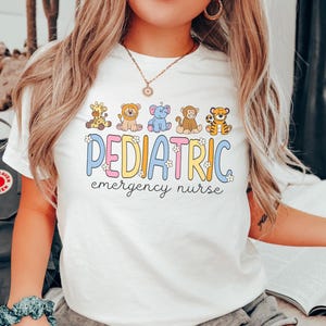 May include: White t-shirt with a colorful graphic that says "PEDIATRIC emergency nurse". The graphic features a line of cartoon animals including a giraffe, lion, elephant, monkey, and tiger.