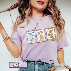 May include: Orchid-colored t-shirt featuring three framed illustrations with cartoon characters and text. The illustrations include a pig, Winnie the Pooh, and a cat, with phrases like "helping you grow your own way" and "Speech Therapy."