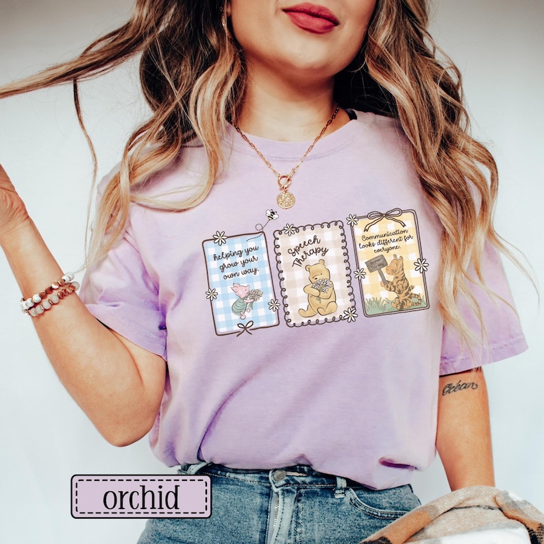 May include: Orchid-colored t-shirt featuring three framed illustrations with cartoon characters and text. The illustrations include a pig, Winnie the Pooh, and a cat, with phrases like "helping you grow your own way" and "Speech Therapy."