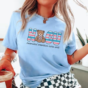 Puede incluir: Camiseta azul claro con un gr&aacute;fico de un osito de peluche y el texto "NICU unidad de cuidados intensivos neonatales".