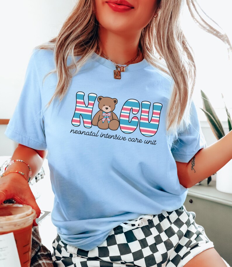 Puede incluir: Camiseta azul claro con un gr&aacute;fico de un osito de peluche y el texto "NICU unidad de cuidados intensivos neonatales".