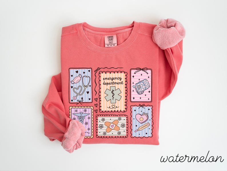 Pode incluir: Uma camisola coral com gola redonda e mangas compridas. A frente apresenta um design de seis ilustra&ccedil;&otilde;es emolduradas de s&iacute;mbolos m&eacute;dicos, incluindo um estetosc&oacute;pio, uma mala m&eacute;dica e um penso. A palavra "emergency department" tamb&eacute;m &eacute; exibida.
