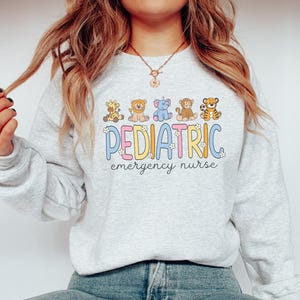 May include: A light gray sweatshirt with a graphic of cartoon animals and the text "Pediatric emergency nurse".