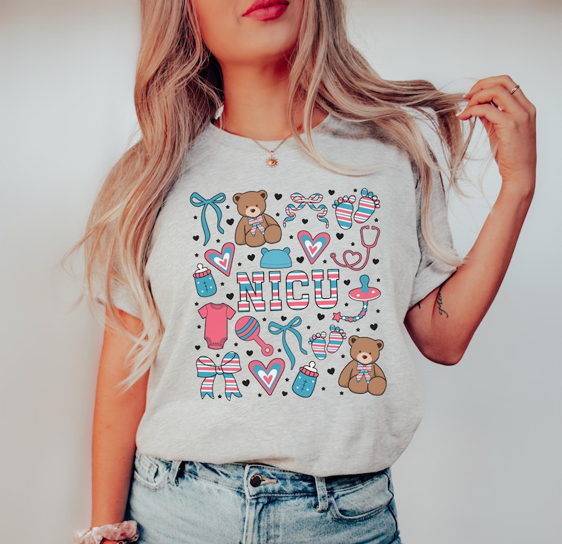 May include: A gray t-shirt with a colorful design featuring the word "NICU" surrounded by baby-themed icons like teddy bears, hearts, pacifiers, and footprints.