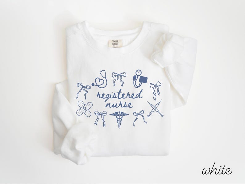 May include: White long-sleeve sweatshirt with a navy blue graphic design. The design includes medical symbols such as a stethoscope, band-aid, and caduceus, along with the words "registered nurse". The word "white" is written in the bottom right corner.