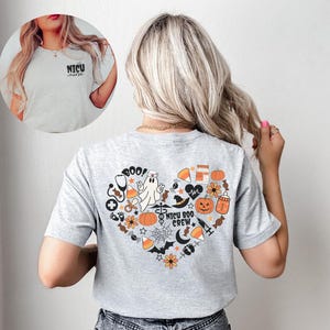 May include: A light gray t-shirt with a heart-shaped Halloween-themed graphic on the back, featuring pumpkins, a ghost, and the text "NICU BOO CREW". The front of the shirt has the text "NICU nurse".