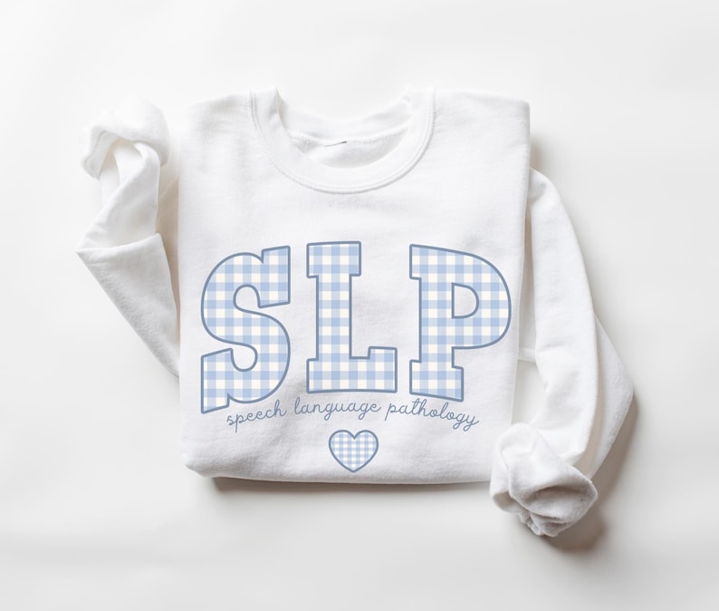 May include: White sweatshirt with a blue and white checkered design that spells out "SLP" and the text "speech language pathology" below. A small blue heart is centered below the text.