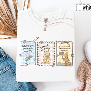 May include: White t-shirt with three framed illustrations featuring Winnie the Pooh characters. The frames contain text: "helping you grow your own way," "Speech Therapy," and "Communication looks different for everyone."