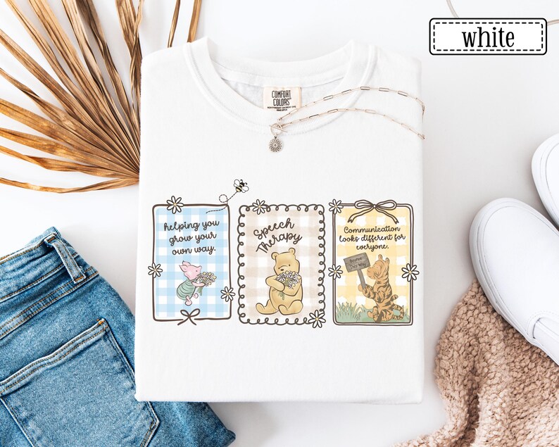 May include: White t-shirt with three framed illustrations featuring Winnie the Pooh characters. The frames contain text: "helping you grow your own way," "Speech Therapy," and "Communication looks different for everyone."
