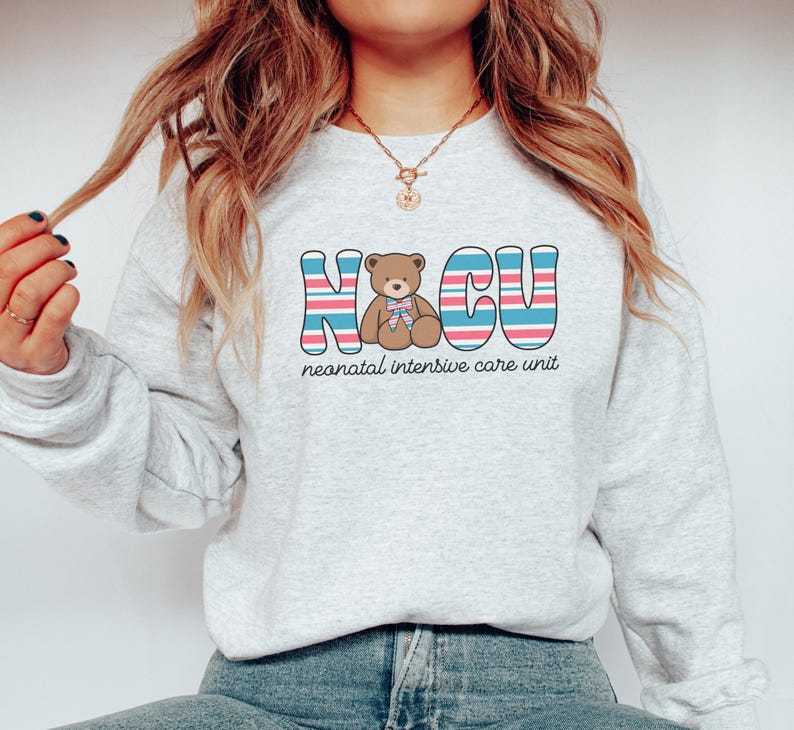 Puede incluir: Una sudadera gris con un gr&aacute;fico colorido de un osito de peluche y el texto "NICU unidad de cuidados intensivos neonatales".