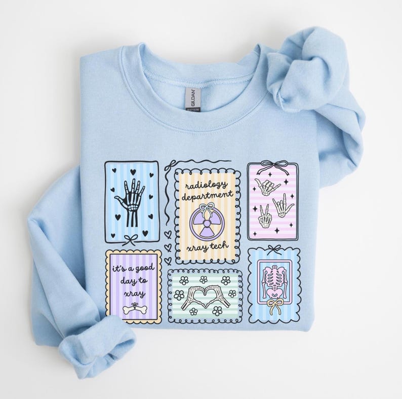 May include: Light blue sweatshirt with multiple framed illustrations. The illustrations include a hand, the words "radiology department" and "xray tech", a heart made of flowers, and a skeleton. The sweatshirt has the text "It's a good day to xray".
