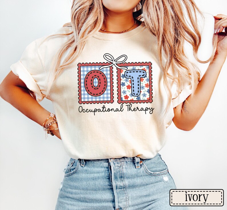 May include: Ivory-colored t-shirt featuring the letters "OT" in decorative postage stamp designs. The "O" is red with a blue gingham background, and the "T" is blue with a floral background. The words "Occupational Therapy" are printed below.