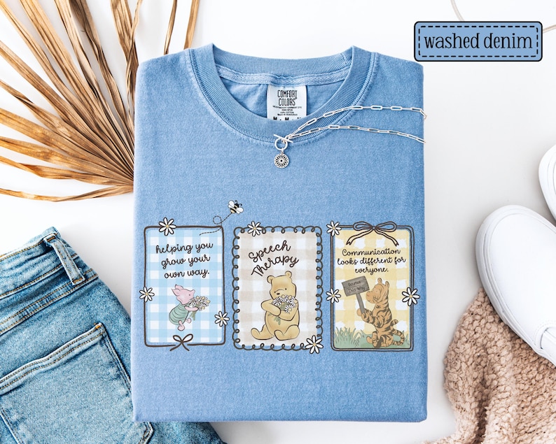 May include: Light blue "washed denim" Comfort Colors t-shirt with Winnie the Pooh characters and the phrases "helping you grow your own way", "Speech Therapy", and "Communication looks different for everyone". A silver necklace is draped on the shirt.