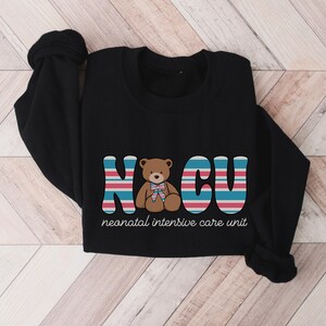 Puede incluir: Camiseta negra de manga larga con un gr&aacute;fico de un osito de peluche y el texto "NCU neonatal intensive care unit".