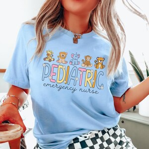 May include: A light blue t-shirt with a graphic of a line of cartoon animals and the text "PEDIATRIC emergency nurse".