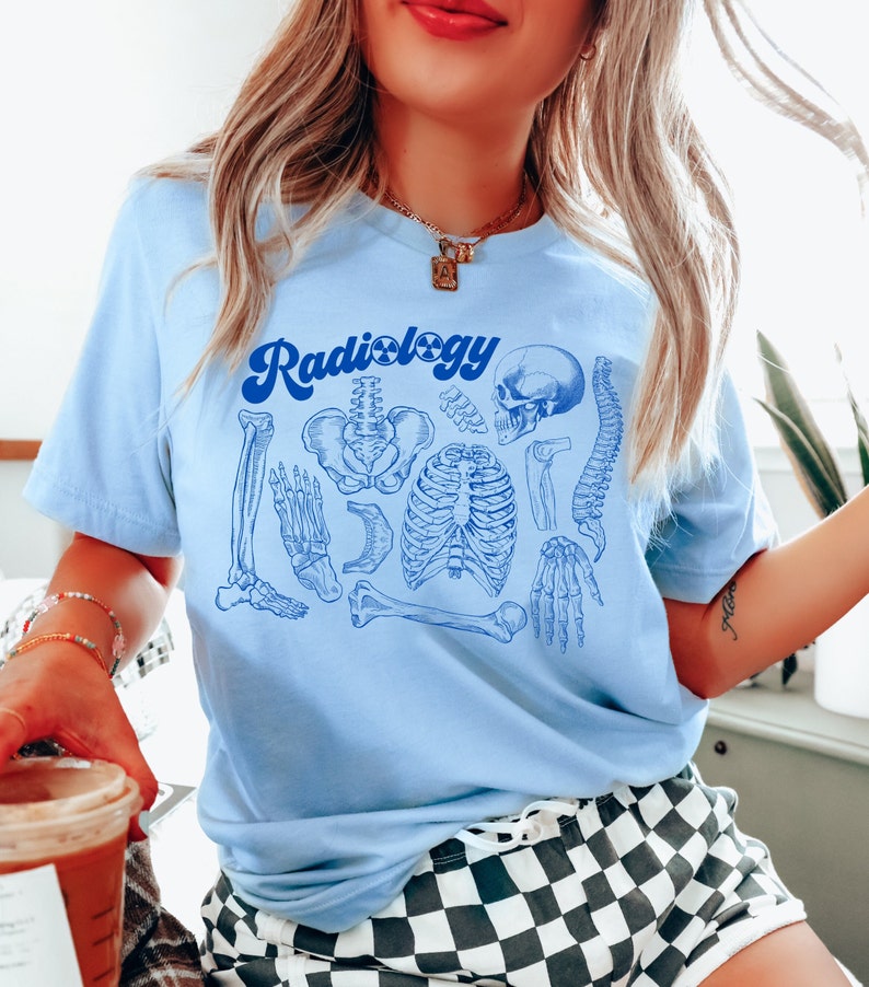 May include: Light blue t-shirt with a blue graphic of human skeletal anatomy and the word "Radiology" in a retro font. The design includes illustrations of bones, a skull, and the spine.