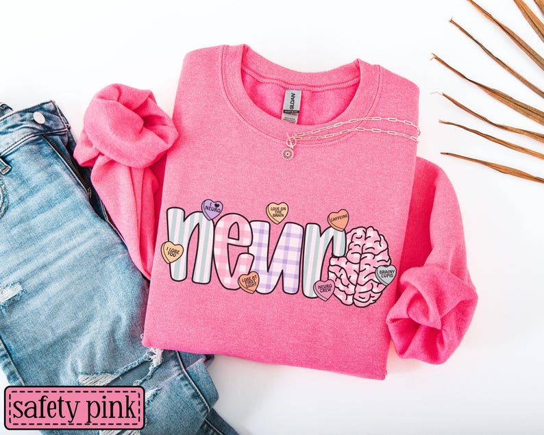 May include: A safety pink sweatshirt with the word "neuro" in a playful font, decorated with candy hearts and a brain graphic. The sweatshirt is paired with blue jeans and a necklace.