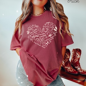 May include: Brick-colored t-shirt featuring a heart-shaped design with the words "nicu nurse" and other text and illustrations. The shirt has short sleeves and a relaxed fit. The word "brick" is written in the upper right corner.
